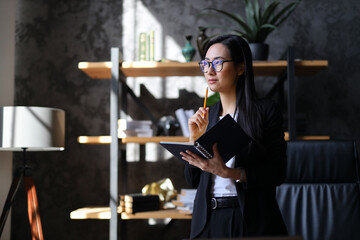 A young, professional Asian businesswoman in a modern office, confidently managing her career with...