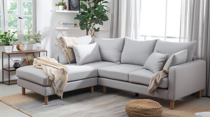Fototapeta premium modern Scandinavian corner sofa in light grey color with pillows and blanket against white wall with shelf, carpet on the floor, window with curtains, plants on shelves, cozy home interior design