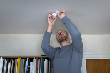 Low angle view of man installing smoke detector on ceiling at home