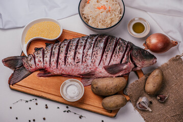 Fresh carp fish on a wooden board, cleaned, before cooking. Fermented cabbage, potatoes, onions, sea salt, olive oil, corn grits. Ingredients. Recipe