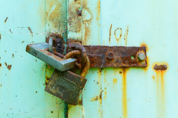 A detailed close-up of two rusty padlocks securing an old, weather-worn metal door, symbolizing security, age, and decay.