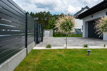 A modern panel fence in anthracite color, visible sliding gate to the garage and a garbage place in...