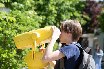 a boy looks through a yellow stationary field view binocular - binoscope, in the park.