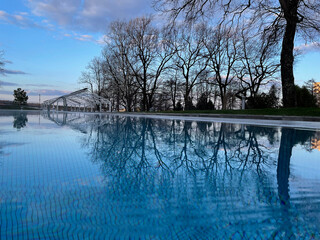 An outdoor swimming pool at dawn, a haze over the water under a blue sky.