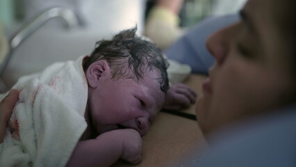 Newborn baby crying for the first time right after birth resting on mother's chest, mother and...