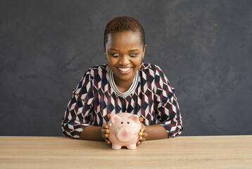 African American woman with a crazy look and a smile looks at a piggy bank in the shape of a pig....