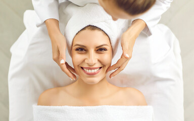 Cheerful young woman enjoying facial treatment at spa salon or beauty parlor. Top overhead view...