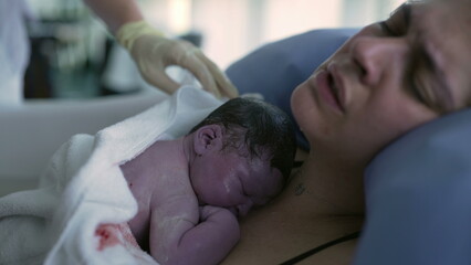 Real life childbirth, mother's expression holding her newborn baby right after birth laid in...