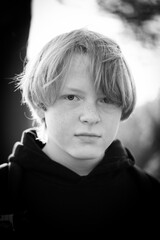 A monochrome portrait depicts a solemn young boy with blonde hair wearing a hoodie, captured...