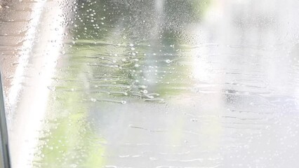 Washing windows. Home cleanliness care. Soap solution is splashed on the window. Clear glass. Scraper for cleaning windows. The housewife washes the window. Vertical video.