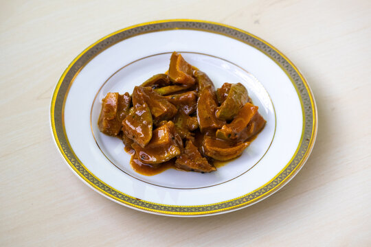 Delicious homemade mango pickle or aam er achar on a white plate on a wooden background.