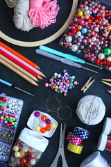 Colorful beads, coloring pencils, glitter, needles, string, hoop, tape and scissors on dark...