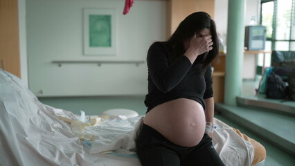 Pregnant woman suffering from contractions during pre labor at clinic covering face in pain,...