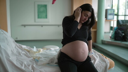 Pregnant woman suffering from contractions during pre labor at clinic covering face in pain,...