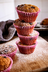 Tower of fresh banana/chocolate chip muffins dusted with powder sugar on vintage cutting board and tray
