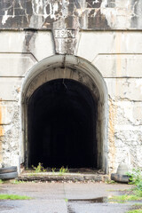 The tunnel entrance has overgrown plants, aged concrete, and abandoned tires, depicting neglect and decay