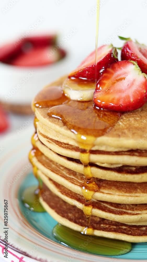 Wall mural pouring maple syrup on a stack of pancakes topped with fresh strawberries and bananas for breakfast.