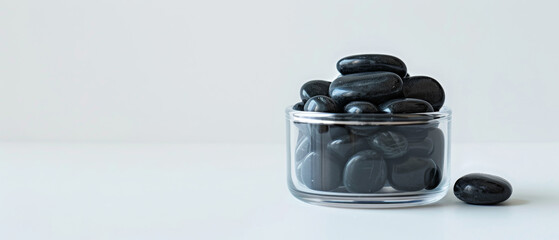 Black stones in a clear glass jar, placed on a pure white background to create a highcontrast and minimalist look