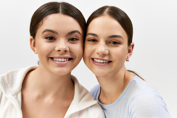 Two pretty, sporty, and brunette teenage girls strike a pose together on a grey studio background, exuding confidence and camaraderie.