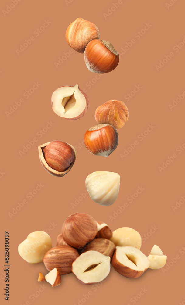 Wall mural Many fresh hazelnuts falling on light brown background