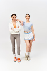 Teenage brunettes, best friends, stand side by side in sportswear against grey backdrop, exuding energy and camaraderie.