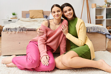 Two stylish young women in casual attire sitting on the floor posing together for a fashionable shot.