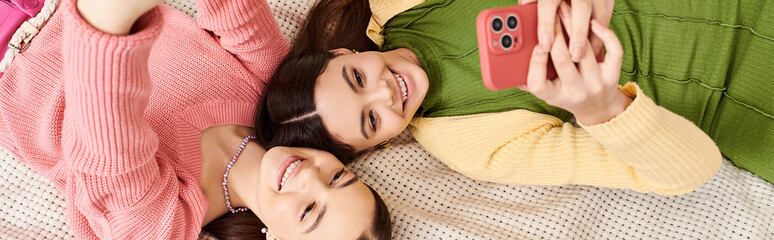 Two stylish young women in casual clothes, peacefully laying side by side on a comfortable bed at home.