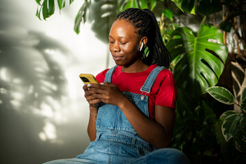 Serene relaxed african american woman in earphones look at screen mobile phone, listen music or...