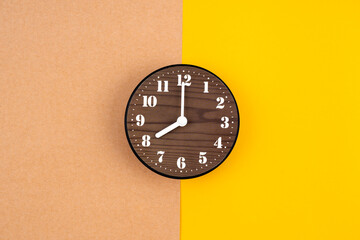 Wooden clock placed in middle of yellow background.