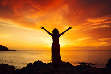 Silhouette of a woman with arms raised standing by a serene lake at sunset, surrounded by mountains, embracing the beauty and tranquility of nature