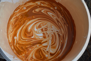 White acrylic paint with brown dye in a bucket.