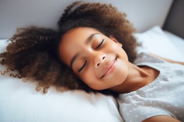 A young girl with curly hair is sleeping on a bed. She is smiling and she is very happy