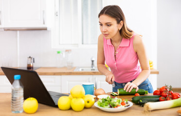 Woman cook reads the recipe in laptop and cooks salad in kitchen