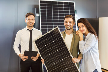 Portrait of a happy solar energy consultant standing with a family couple in a shop. Discuss...