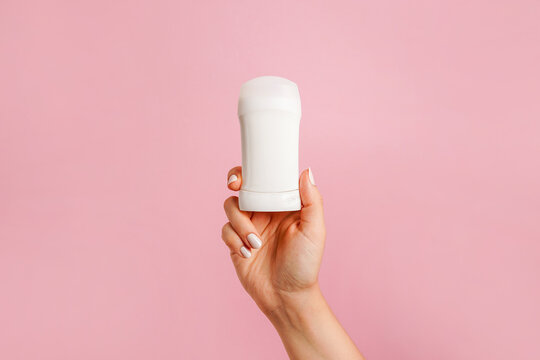 Hand holding white body deodorant on pink background