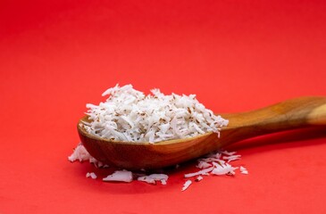 Grated Coconut White Flesh in a Wooden Spoon Isolated on Red Background with Copy Space