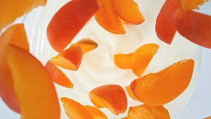 Fresh apricots pieces falling into cream, top down view