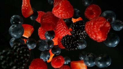 Fresh pieces of berries falling into water, top down view, black background