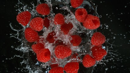 Fresh pieces of raspberries falling into water, top down view, black background