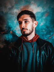 Young Man in Leather Jacket Posing Against Artistic Blue and Black Wall at Night
