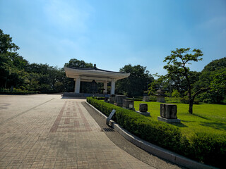 Fototapeta premium A park with a white pavilion and a stone wall. The park is surrounded by trees and has a grassy area