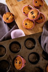 Fresh banana/chocolate chip muffins on vintage cutting board with muffin tray and sieve