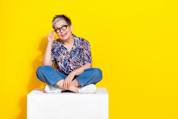 Full length photo of lovely senior lady sit cube look empty space dressed stylish colorful garment isolated on yellow color background