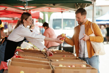 Giving apples. Man is buying products on the street market or bazaar from woman