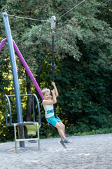 A smiling little boy is rolling on a tightrope chassis in nature in the summer. Vertical photo