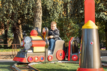Amusement park entertainment red toy train locomotive.Little boy wants to take a ride on electric children transport.