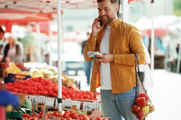 Talking by phone. With shopping list. Handsome man is on the street market or bazaar