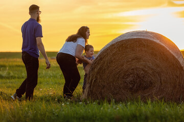Playful family on a green meadow near a hay roll against the background of the yellow evening sun...