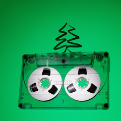 Square photo with old audio cassette and Christmas tree from tape on green background. The photo is...