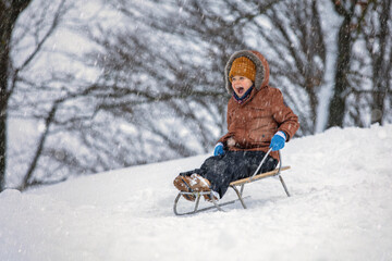 A little boy, a happy child rides in a sleigh in the snow